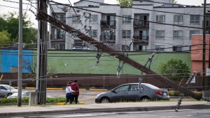 People walk away along Merivale Road, after power lines and utility poles came down onto the roadway during a major storm, forcing motorists to remain in their vehicles until crews determined it was safe to leave, on Merivale Road in Ottawa, on Saturday, May 21, 2022. (Justin Tang/THE CANADIAN PRESS)