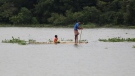 A man and a child travel on a wooden plank through flood waters in Bagha area in Sylhet, Bangladesh, Monday, May 23, 2022. (AP Photo)