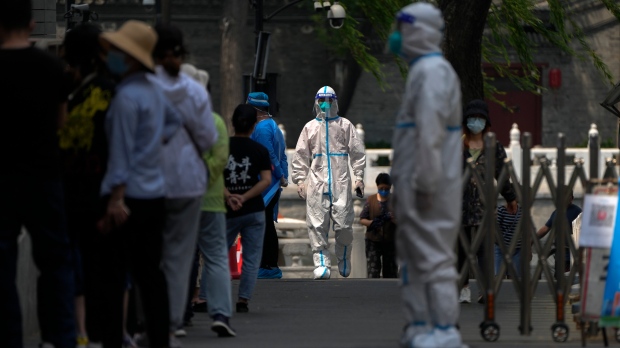 Health workers in protective gear stand while watching residents line up for public COVID-19 testing in Beijing on May 24, 2022. (AP Photo/Andy Wong)