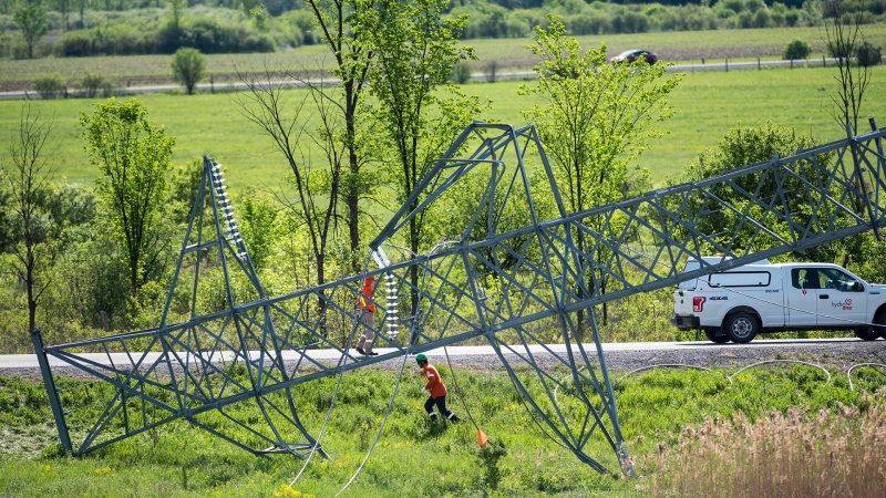 A utility worker passes the top segment of a transmission tower, lying on the ground, after it was damaged in Saturday’s major storm in Ottawa, on Tuesday, May 24, 2022. (Justin Tang/THE CANADIAN PRESS)