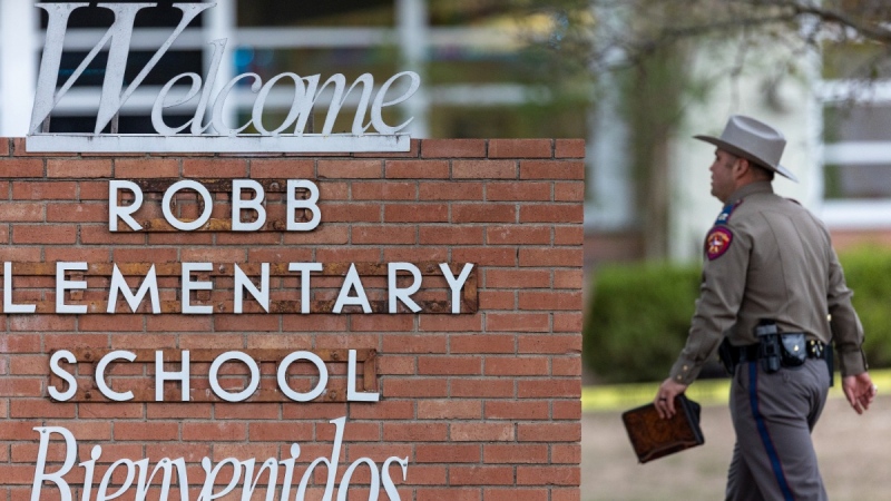 A state trooper walks past the Robb Elementary School sign in Uvalde, Texas, on May 24, 2022. (William Luther / The San Antonio Express-News via AP) 