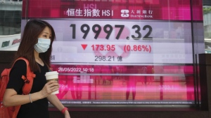 A woman wearing a face mask walks past a bank's electronic board showing the Hong Kong share index in Hong Kong, May 26, 2022. (AP Photo/Kin Cheung)