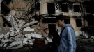 Two men walk in front of a damage building ruined by attacks in Hostomel, outskirts Kyiv, Ukraine, May 26, 2022. (AP Photo/Natacha Pisarenko)