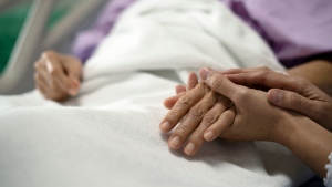 A senior sits in a bed holding a hand in a stock photo. (Getty Images) 