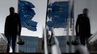A man carries a cycling helmet as he walks by EU flags outside EU headquarters in Brussels on Oct. 28, 2020. (AP Photo/Virginia Mayo)