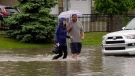 Two people walk across a flooded street in Saskatoon's Stonebridge neighbourhood on June 20, 2022. (Chad Hills/CTV News)