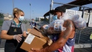 Los Angeles Unified School District food service worker Marisel Dominguez, left, distributes free school lunches and a weekend box to parent Ernesto Cortes on Friday, July 16, 2021, at the Liechty Middle School in Los Angeles. (AP Photo/Damian Dovarganes)