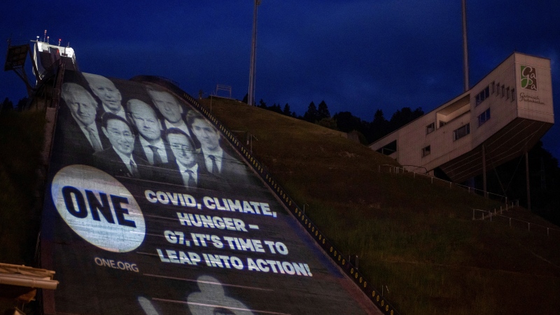 The projection with the likenesses of the 7 heads of government and the words "Covid, Climate, Hunger - G7, It's Time to Leap into Action!" is cast onto the Great Olympic Hill in Garmisch-Partenkirchen, Germany, Saturday, June 25, 2022. (Peter Kneffel/dpa via AP)