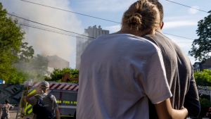 A couple embrace as they look at smoke billowing the air from residential buildings following explosions, in Kyiv, Ukraine, Sunday, June 26, 2022. Several explosions rocked the west of the Ukrainian capital in the early hours of Sunday morning, with at least two residential buildings struck, according to Kyiv mayor Vitali Klitschko. (AP Photo/Nariman El-Mofty)
