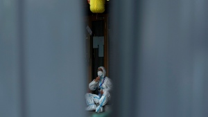 A worker in protective suit takes a break outside a locked down restaurant barricaded with metal barriers as part of COVID-19 controls in Beijing, June 26, 2022. (AP Photo/Andy Wong)