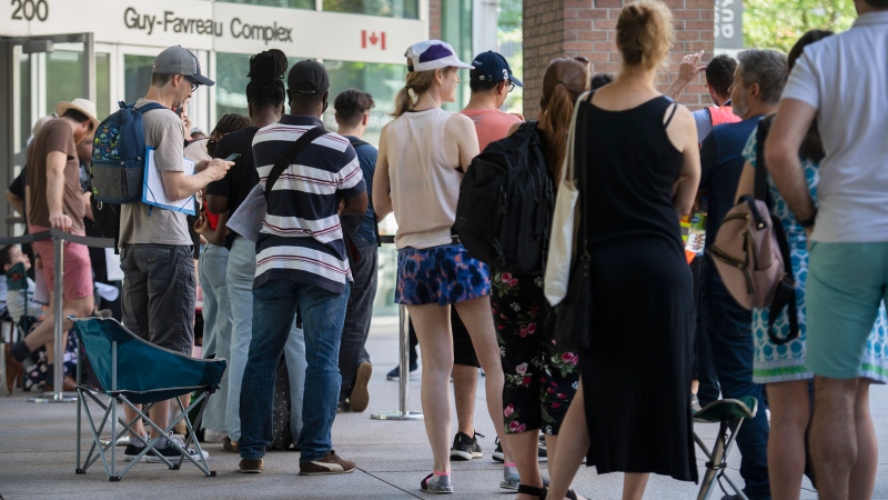 People line up outside the Guy Favreau federal building while waiting to apply for a passport in Montreal, Sunday, June 26, 2022. (THE CANADIAN PRESS/Graham Hughes)
