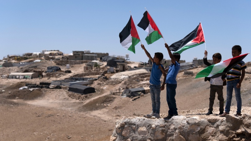 Palestinian kids wave the national flags as they welcome Palestinian Prime Minister Mohamed Shtayyeh at the West Bank village of Masafer Yatta, on June 26, 2022. (Majdi Mohammed / AP) 