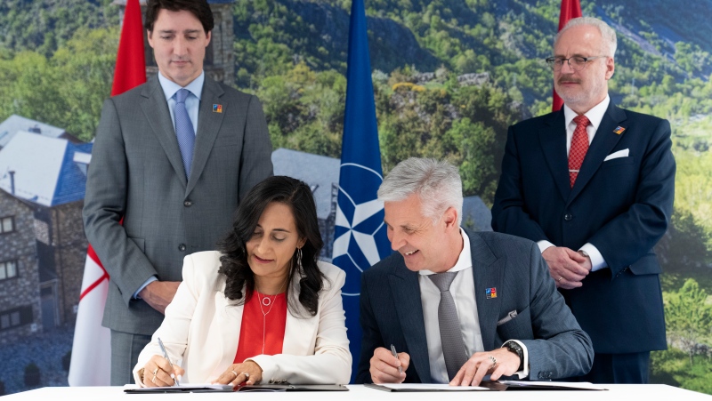 Latvian Minister of Defence Artis Pabriks and Canadian counterpart Anita Annad sign an agreement as Prime Minister Justin Trudeau and Latvian President Egils Levits look on at the NATO Summit in Madrid on Wednesday, June 29, 2022. THE CANADIAN PRESS/Paul Chiasson