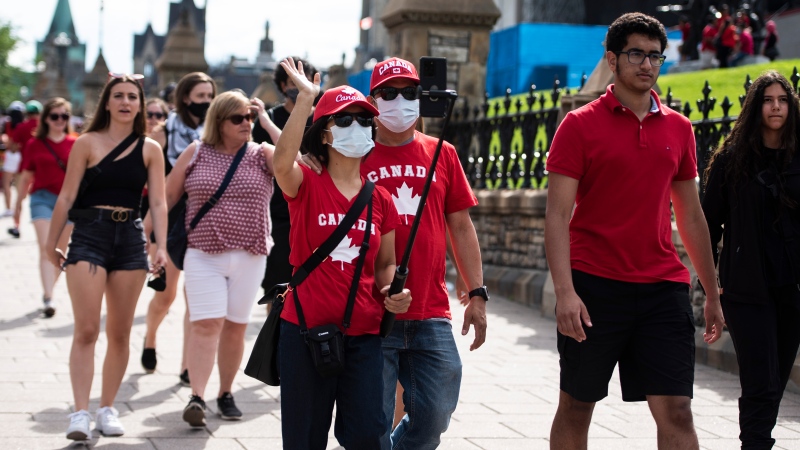 People wear the maple leaf as they wave into a camera phone as they walk along Wellington Street in Ottawa on Canada Day, Thursday, July 1, 2021. THE CANADIAN PRESS/Justin Tang