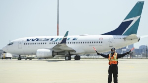 Airline groundcrew work as a grounded Westjest plane sits on the tarmac at Pearson International Airport during the during the COVID-19 pandemic in Toronto on Tuesday, April 27, 2021. The chief executive of WestJet Airlines Ltd. says it is flying 32 per cent fewer flights in and out of Toronto Pearson International Airport in July than it did in 2019. THE CANADIAN PRESS/Nathan Denette