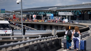 Travellers arrive on foot at Roissy-Charles de Gaulle airport while airport workers demonstrate, left, Friday, July 1, 2022 at Roissy airport, north of Paris. (AP Photo/ Thomas Padilla)