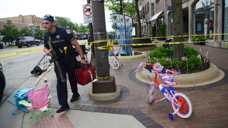 A police officer walks past a child's bicycle that was left along the parade route a block away from the scene of a shooting involving multiple victims that took place at the Highland Park, Ill., Fourth of July parade, July 4, 2022. (Joe Lewnard//Daily Herald via AP)