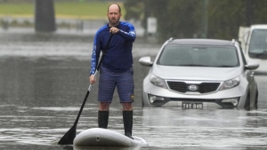 A man paddles on a stand-up paddle board through a flooded street at Windsor on the outskirts of Sydney, Australia, July 5, 2022. (AP Photo/Mark Baker)