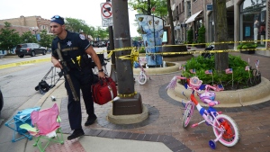 A police officer walks past a child's bicycle that was left along the parade route a block away from the scene of a shooting involving multiple victims that took place at the Highland Park, Ill., Fourth of July parade Monday, July 4, 2022. (Joe Lewnard//Daily Herald via AP)