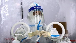 A worker wearing a protective suit waits to administer a COVID-19 test at a coronavirus testing site in Beijing, July 6, 2022. (AP Photo/Mark Schiefelbein)