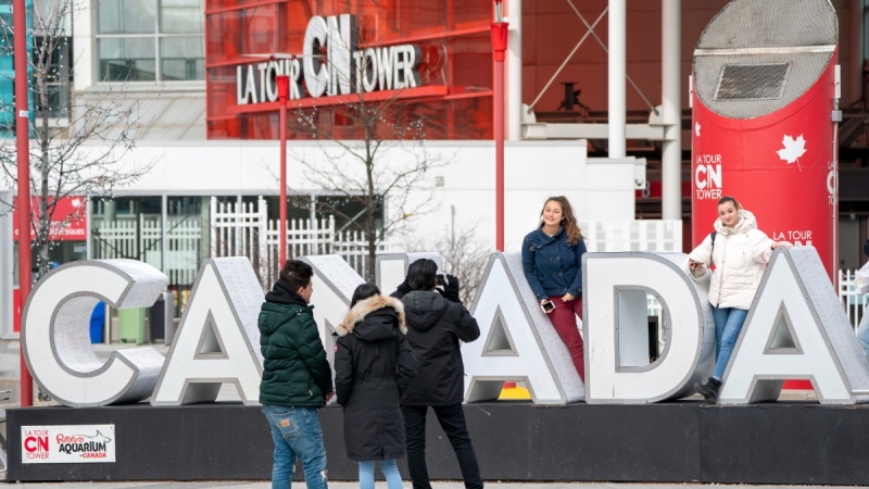 Tourists pose for photos at the base of the CN Tower in Toronto, March 14, 2020. THE CANADIAN PRESS/Frank Gunn