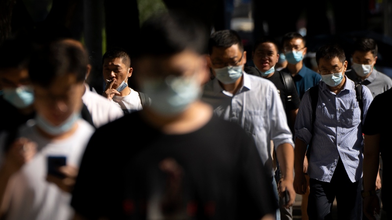 Commuters wearing face masks walk along a street in the central business district in Beijing, July 7, 2022. (AP Photo/Mark Schiefelbein)