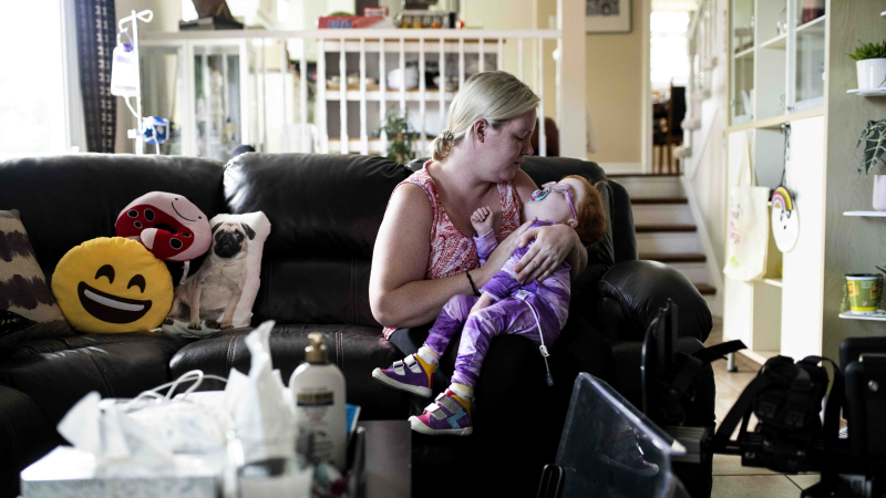 Amanda Jollymore rocks her daughter Mia, 2, who has an unknown genetic syndrome along with other diagnosed medical issues, as they sit on the couch at their home in Ottawa, on Monday, June 27, 2022. (Justin Tang /THE CANADIAN PRESS)