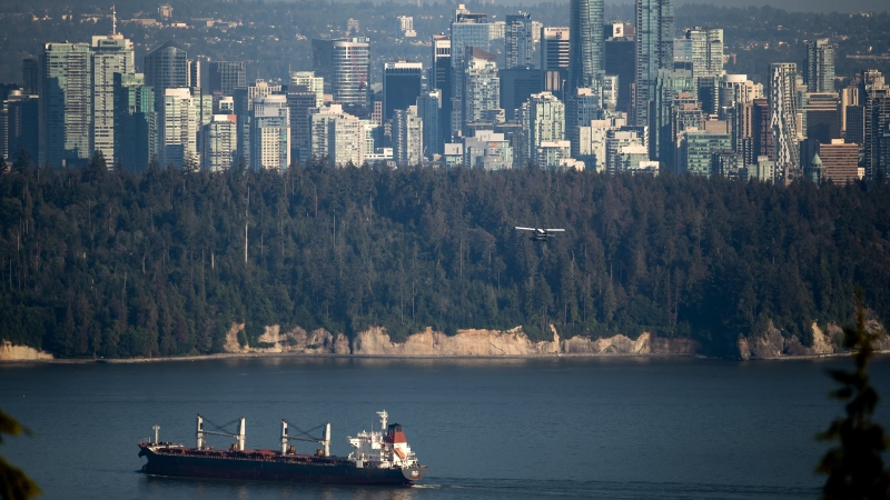A bulk carrier cargo ship travels into port as a Harbour Air seaplane flies towards Stanley Park and the downtown skyline, in Vancouver, on Wednesday, July 27, 2022. THE CANADIAN PRESS/Darryl Dyck 