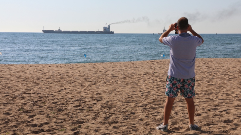 A man takes a picture as the Glory bulk carrier makes its way from the port in Odesa, Ukraine on Aug. 7, 2022. According to Ukraine's Ministry of Infrastructure, the ship under the Marshall Islands' flag is carrying 66 thousand tons of Ukrainian corn. (AP Photo/Nina Lyashonok)