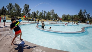 A young boy sprays a water guns at his friends trying to beat the heat at a splash park in Calgary, Alta., Wednesday, June 30, 2021. (THE CANADIAN PRESS/Jeff McIntosh)