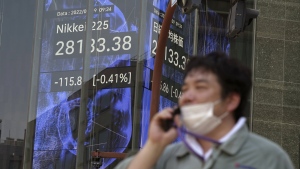 A person wearing a protective mask walks in front of an electronic stock board showing Japan's Nikkei 225 index at a securities firm, Aug. 9, 2022, in Tokyo. (AP Photo/Eugene Hoshiko)