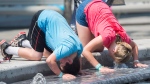 A boy and girl dunk their heads in a water fountain during a heatwave in Montreal, Monday, July 2, 2018. THE CANADIAN PRESS/Graham Hughes