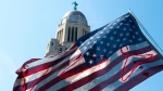 An American flag decorated with coat hangers flies over a crowd of protesters during an Abortion Rights Rally held in front of the Nebraska State Capitol on Monday, July 4, 2022, in Lincoln, Neb. (Kenneth Ferriera/Lincoln Journal Star via AP)