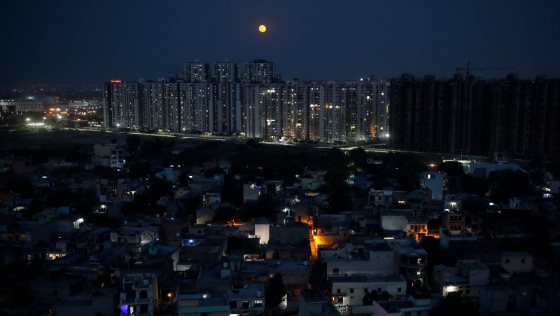 A full moon rises from behind residential buildings in Greater Noida, a suburb of New Delhi, India, May 7, 2020. The Indian government took a step toward their climate goals by passing amendments to an energy conservation bill. (AP Photo/Altaf Qadri, File)