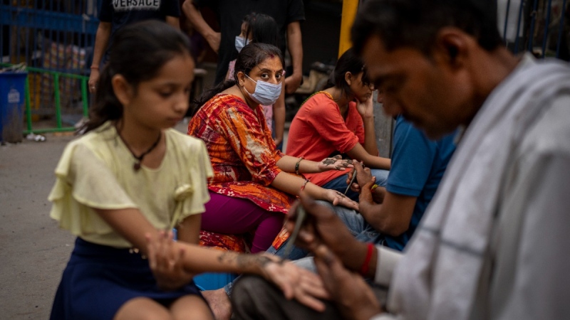 A woman wearing a mask as a precaution against coronavirus gets her hands decorated with henna on the eve of the Hindu festival of Raksha Bandhan in New Delhi, India, on Aug. 11, 2022. (Altaf Qadri / AP) 