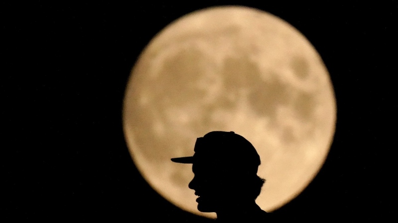 A man is silhouetted against the full moon, Aug. 21, 2021, in Kansas City, Mo. The August full moon is known as the "sturgeon moon." (AP Photo/Charlie Riedel)