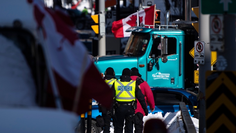 A trucker, in red jacket, is led away by police officers after stepping out of his truck after police surrounded a blockade of vehicles on Rideau Street, on the 22nd day of a protest against COVID-19 measures that has grown into a broader anti-government protest, in Ottawa, on Friday, Feb. 18, 2022. THE CANADIAN PRESS/Justin Tang 