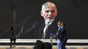 Passengers walk to the departures terminal of Hamid Karzai International Airport in Kabul, Afghanistan, Aug. 14, 2021, past a mural of President Ashraf Ghani, as the Taliban offensive encircled the capital. (AP Photo/Rahmat Gul)