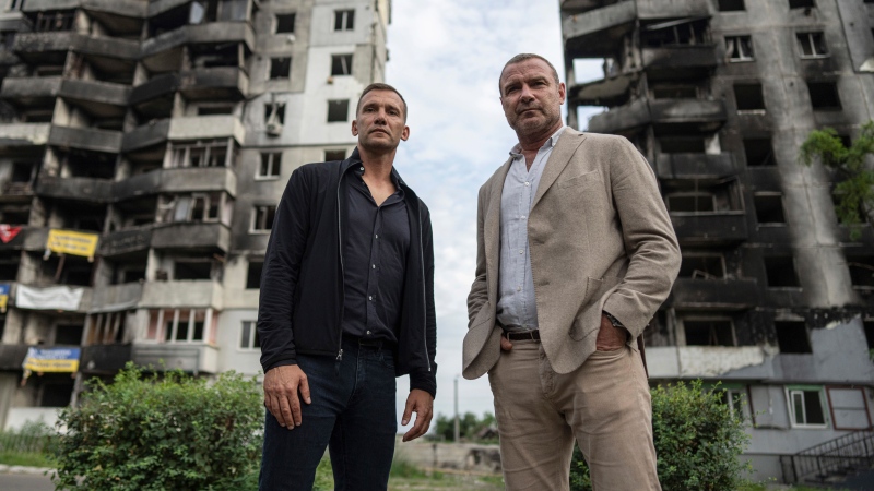 Former striker and coach of the Ukraine national soccer team Andriy Shevchenko, left, and American actor Liev Schreiber stand in front of a house which have been destroyed by Russia bombardment in Borodianka, near Kyiv, Ukraine, on Monday, Aug. 15, 2022. (AP Photo/Evgeniy Maloletka)
