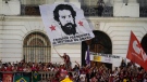 A man unfurls a banner with a message that reads in Portuguese: "The best president in the history of Brazil," emblazoned with an image of a younger version of Brazil's former president Luiz Inacio Lula da Silva, who is running for reelection, during a campaign rally at Cinelandia square, in Rio de Janeiro, Brazil, July 7, 2022. (AP Photo/Silvia Izquierdo, File)