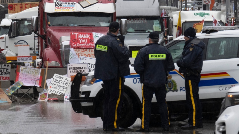 Police officers keep an eye on protest trucks, Feb. 17, 2022 in Ottawa. THE CANADIAN PRESS/Adrian Wyld