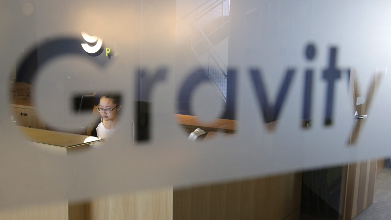 Cary Chin, left, is seen through a sign on the glass door of Gravity Payments, a credit card payment processor based in Seattle, as she works Wednesday, April 15, 2015. (AP Photo/Ted S. Warren)