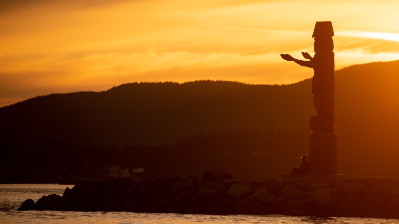 A person is silhouetted while sitting at the foot of the Squamish Nation welcome figure during sunset at Ambleside Beach in West Vancouver, B.C. on Saturday, August 13, 2022. THE CANADIAN PRESS/Darryl Dyck