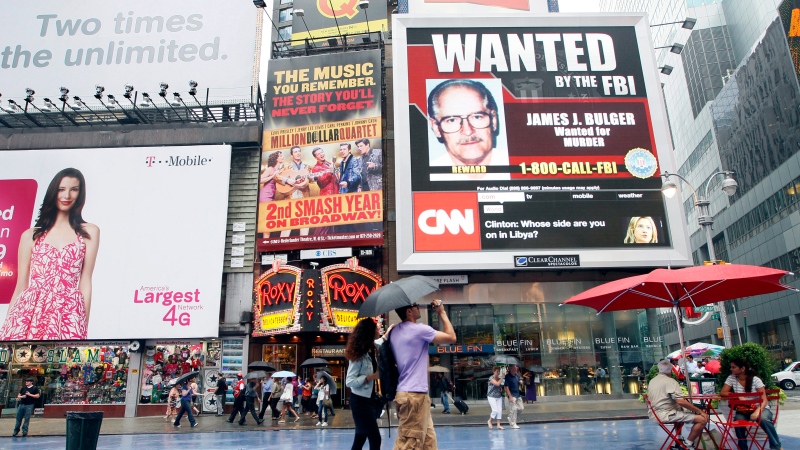 A couple walks past an FBI video looking for mob boss James 'Whitey' Bulger on display in New York's Times Square, Thursday, June 23, 2011. (AP Photo/Mary Altaffer)
