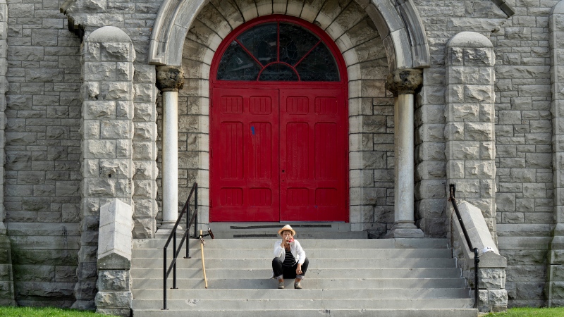 A person sits on the stairs outside a decommissioned church, Thursday, August 18, 2022 in Ottawa. An Ottawa-based group with suspected ties to the 'Freedom Convoy' says it has been threatened with eviction and is ready to take its cause to court in an attempt to set up headquarters in the country's capital. (Adrian Wyld/THE CANADIAN PRESS)
