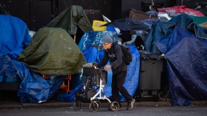 A man using a rolling walker walks on the street past tents setup on the sidewalk at a sprawling homeless encampment on East Hastings Street in the Downtown Eastside of Vancouver, on Tuesday, August 16, 2022. The city's fire chief issued an order last month requiring the tents to be cleared because of an extreme fire safety hazard. THE CANADIAN PRESS/Darryl Dyck