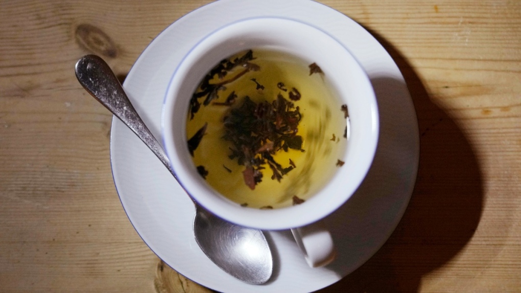 A cup of black tea with a spoon and tea leaves