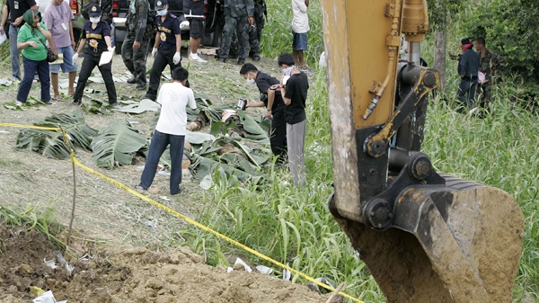 Filipinos look at bodies of massacre victims covered in banana leaves along a hillside grave in Ampatuan, Maguindanao province, southern Philippines on Wednesday, Nov. 25, 2009. (AP / Aaron Favila)