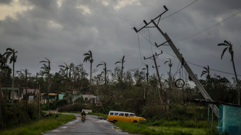 A classic American car drives past utility poles tilted by Hurricane Ian in Pinar del Rio, Cuba, Tuesday, Sept. 27, 2022. (AP Photo/Ramon Espinosa)