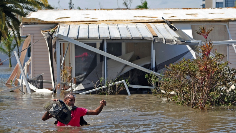 Jonathan Strong holds his vest above the water as he wades through floodwaters while knocking on doors in a flooded mobile home community in Iona, an unincorporated community in Lee County near Fort Myers, Fla., Thursday, Sept. 29, 2022. (Amy Beth Bennett/South Florida Sun-Sentinel via AP) 